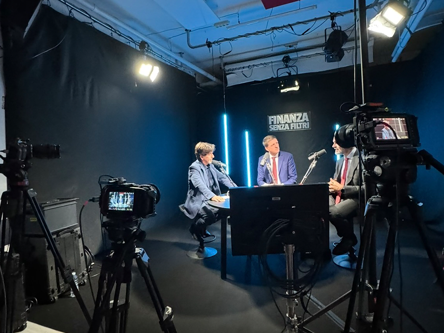 Registrazione video podcast: tre ospiti al tavolo tra camere, microfoni a braccio e retroilluminazione ciano